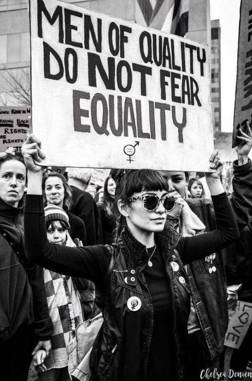 A woman holding a sign reading "men of quality do not fear equality" A woman holding a sign reading "men of quality do not fear equality"