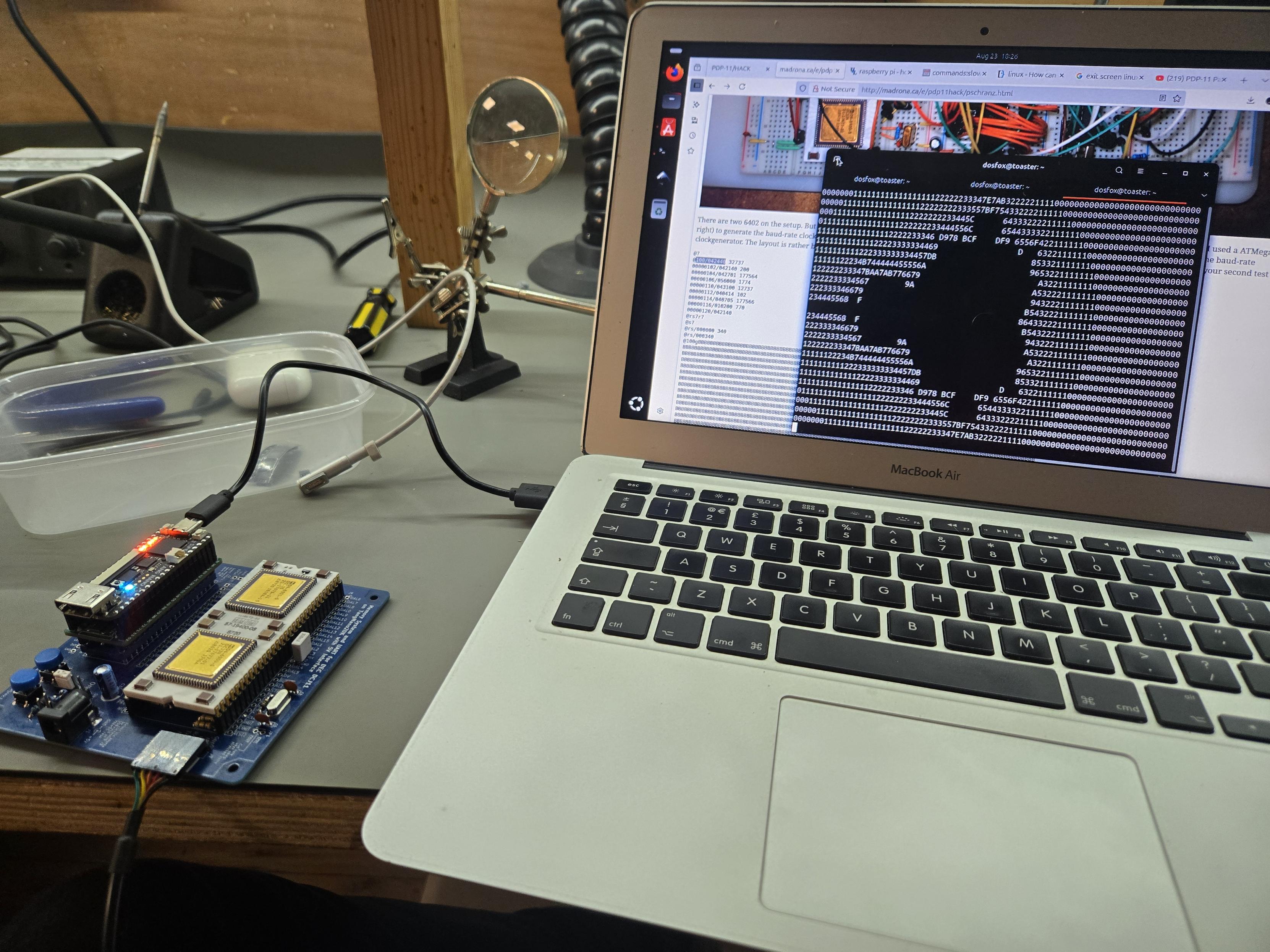 A small blue PCB with a very distinctive white and gold ceramic IC (really two gold ICs on a ceramic carrier) - which is the DEC J11, effectively that's an entire PDP11 on a chip. 

Hooked up to the PDP11 is a Tang Nano 20k 

The system is connected up to a 2011 MacBook air, running Ubuntu. On the display is a terminal emulator - with a very distinctive Mandelbrot set displayed - as computed by the J11