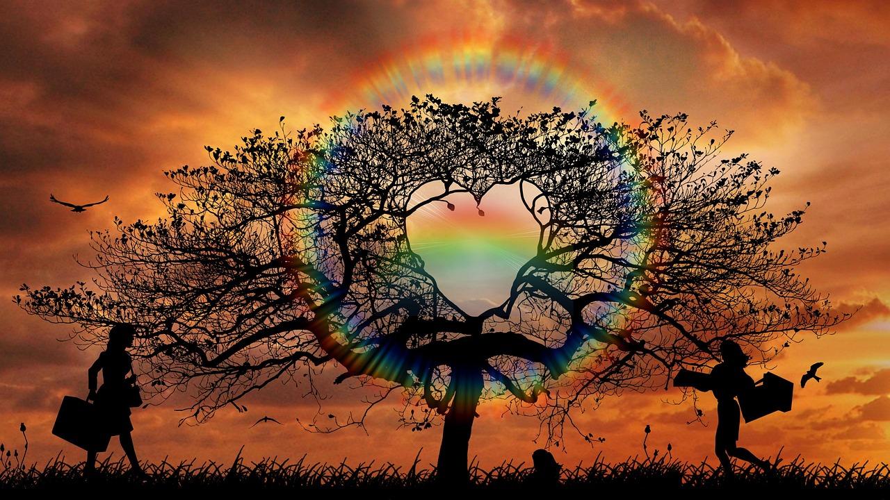 2 women walking towards a tree with a rainbow heart. Behind is a sunset and flying bird. All are silhouettes.
