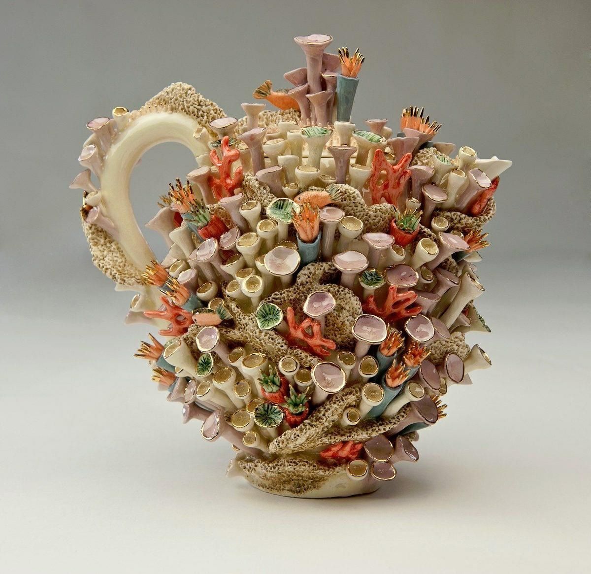 An incredibly intricate teapot in light beige decorated from top to toe as though it's a texturef coral reef