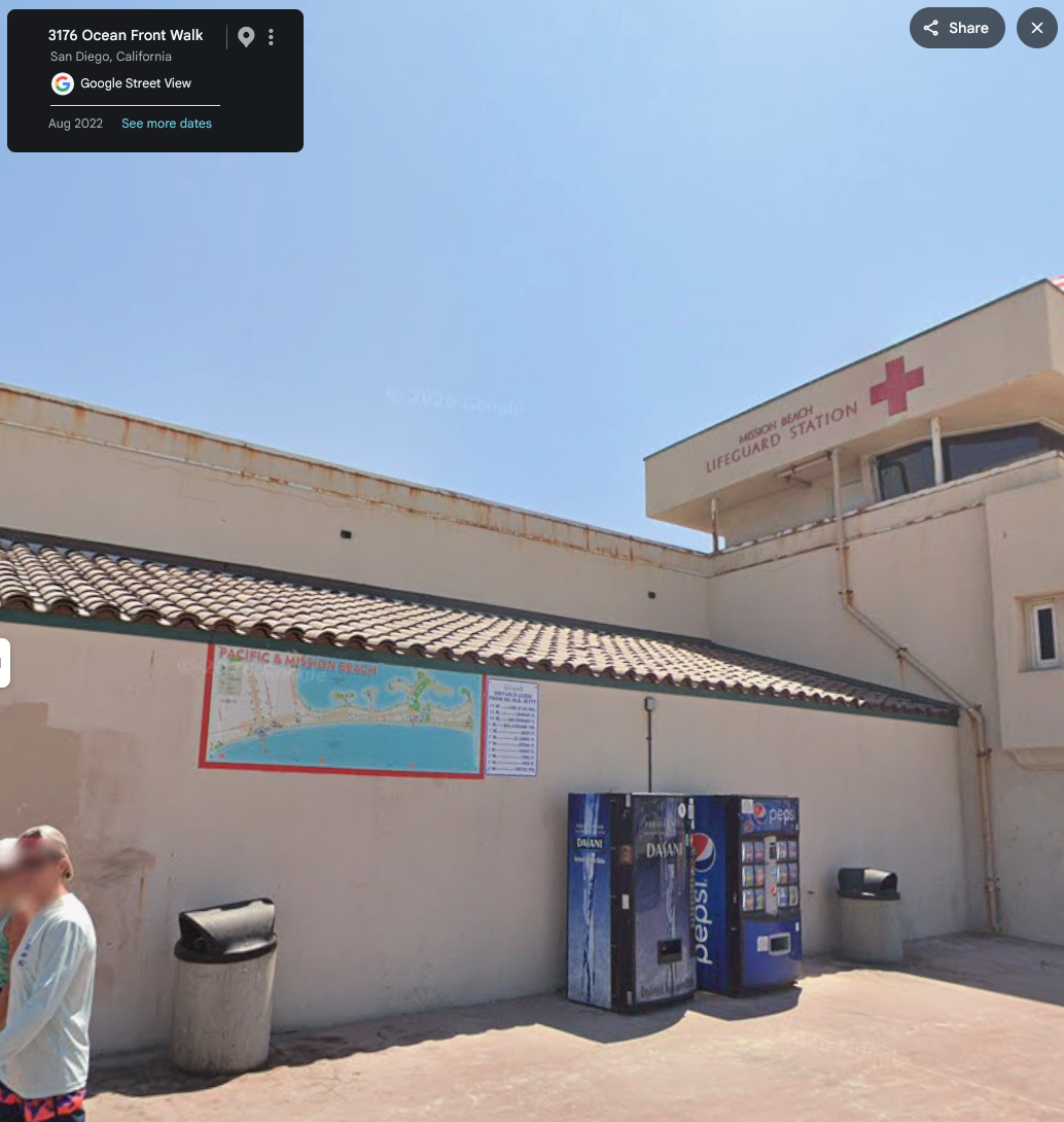 Google street view image showing the Pacific & Mission Beach map on the wall of the Mission Beach Lifeguard station. It is an oddly shaped concrete building with a clay tile roof.