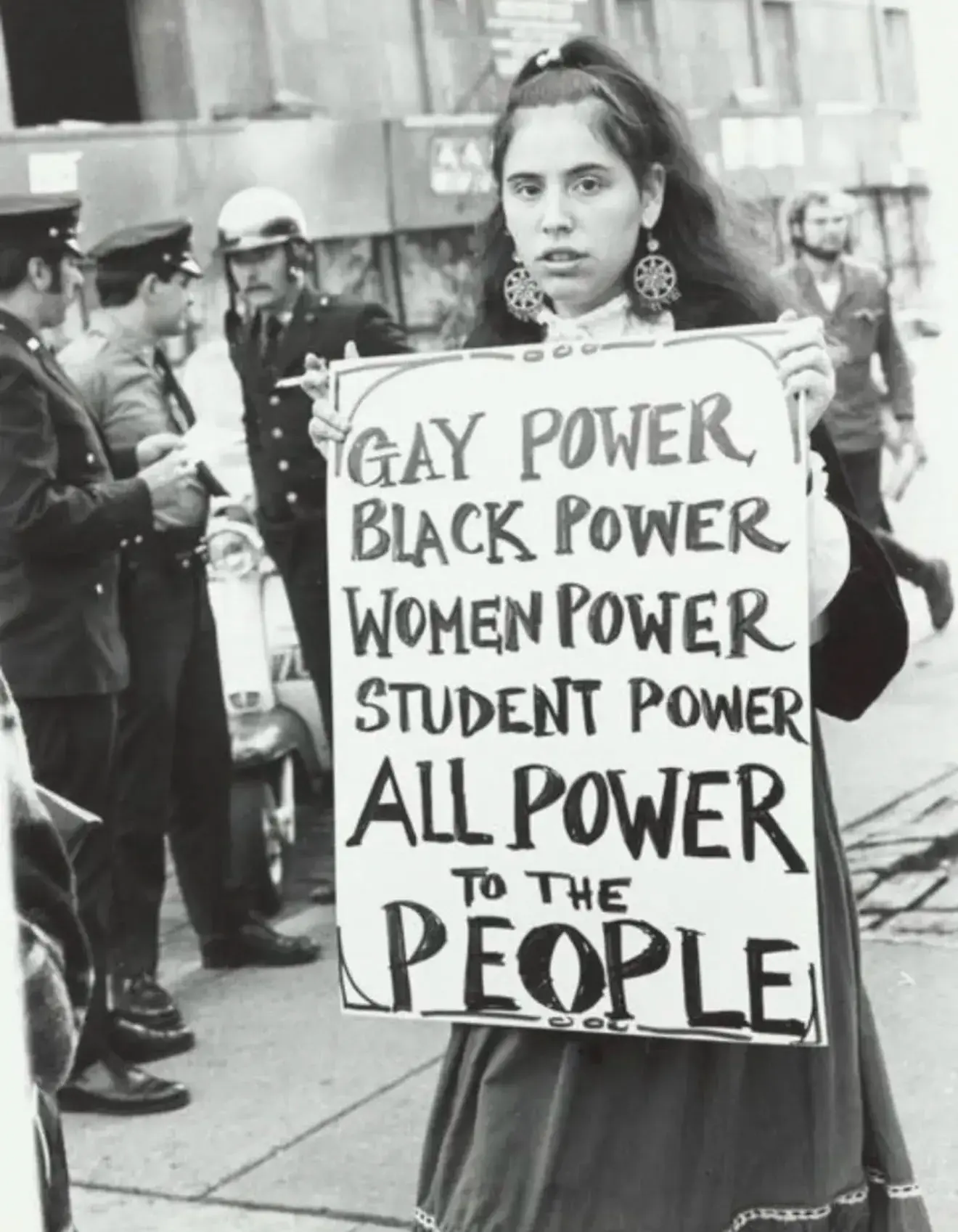 Female protester with the sign - GAY POWER BLACK POWER WOMEN POWER STUDENT POWER 

ALL POWER TO THE PEOPLE