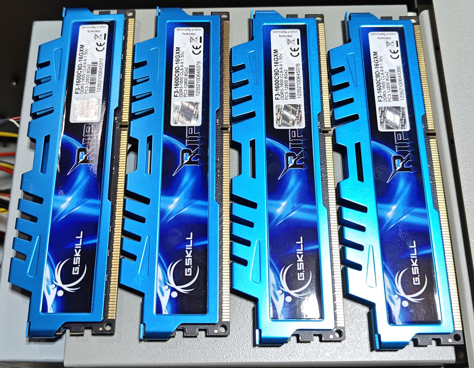 A close-up photograph displays four identical desktop RAM sticks laid out side-by-side on a gray surface. The modules feature bright metallic blue, aggressively styled aluminum heat spreaders under the G.Skill Ripjaws X series line, with comb-like fins along the top edge. Each stick features a prominent white G.SKILL logo near the base. White specification labels are affixed to the top right of each module, showing model number F3-1600C9D-16GXM, indicating DDR3-1600 CL9 memory rated at 1.50 volts, with a capacity of 8 gigabytes per stick, totaling 32 gigabytes of system memory.