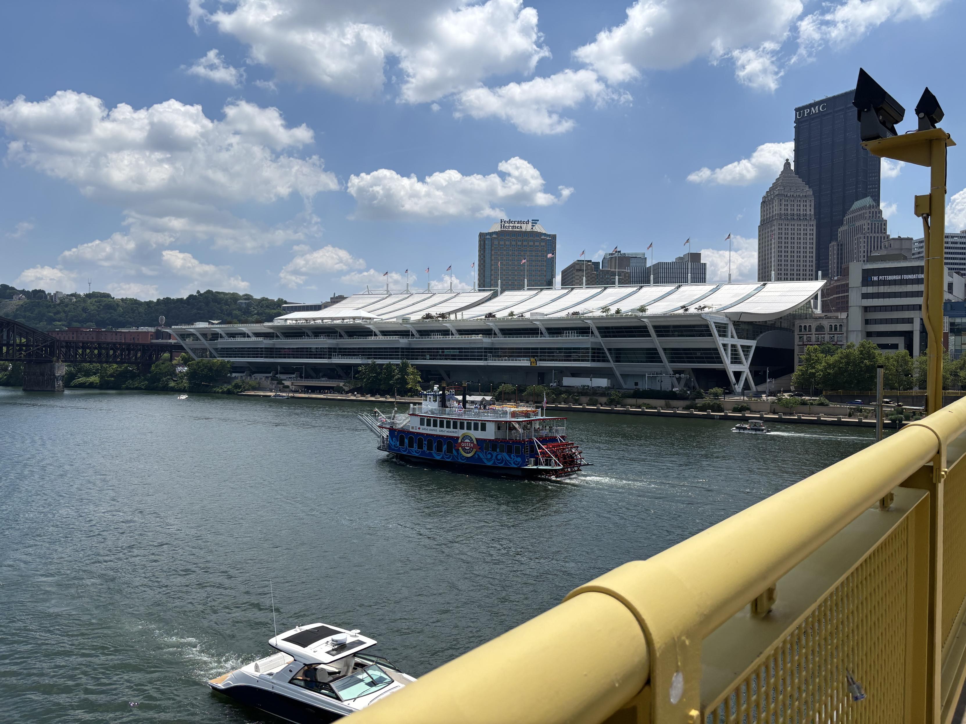 A picture of the David L Lawrence Convention Center in Pittsburgh, taken from a nearby bridge. There’s a furry cruise ship on the river in front of the convention center.