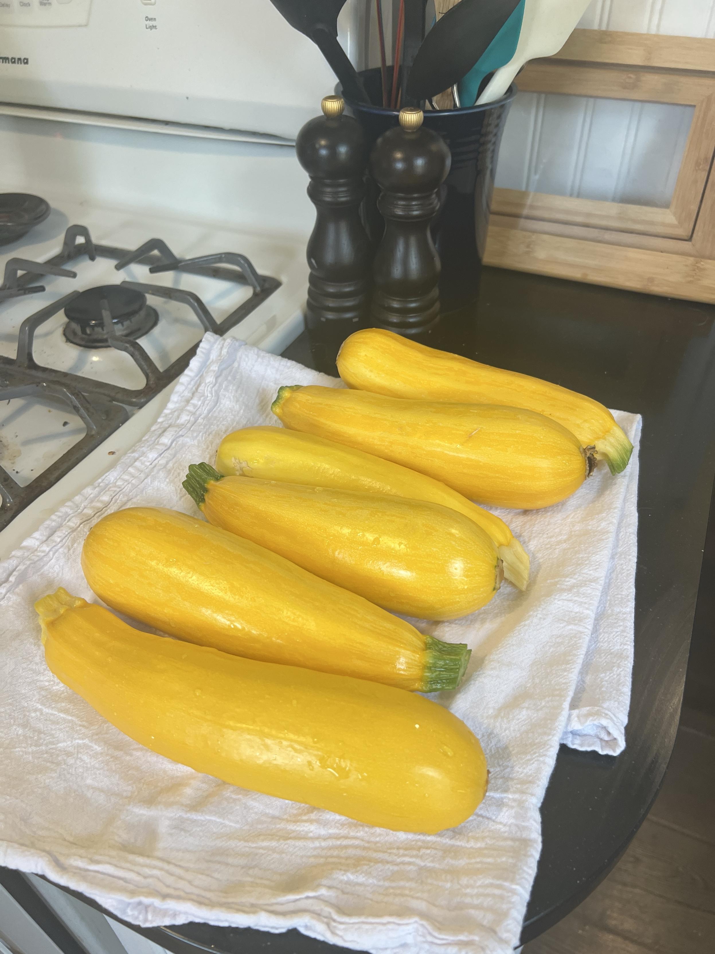 A collection of bright yellow zucchinis arranged on a white cloth, with a stove and kitchenware in the background.