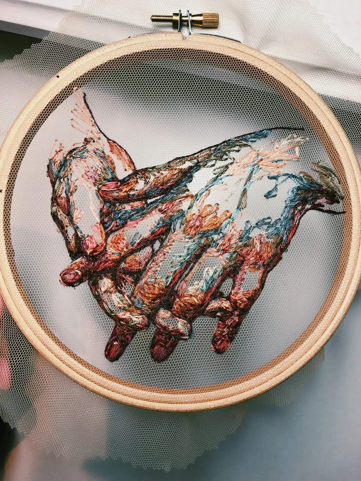 It features intricately embroidered hands with interlocking fingers stitched into a delicate, transparent tulle fabric