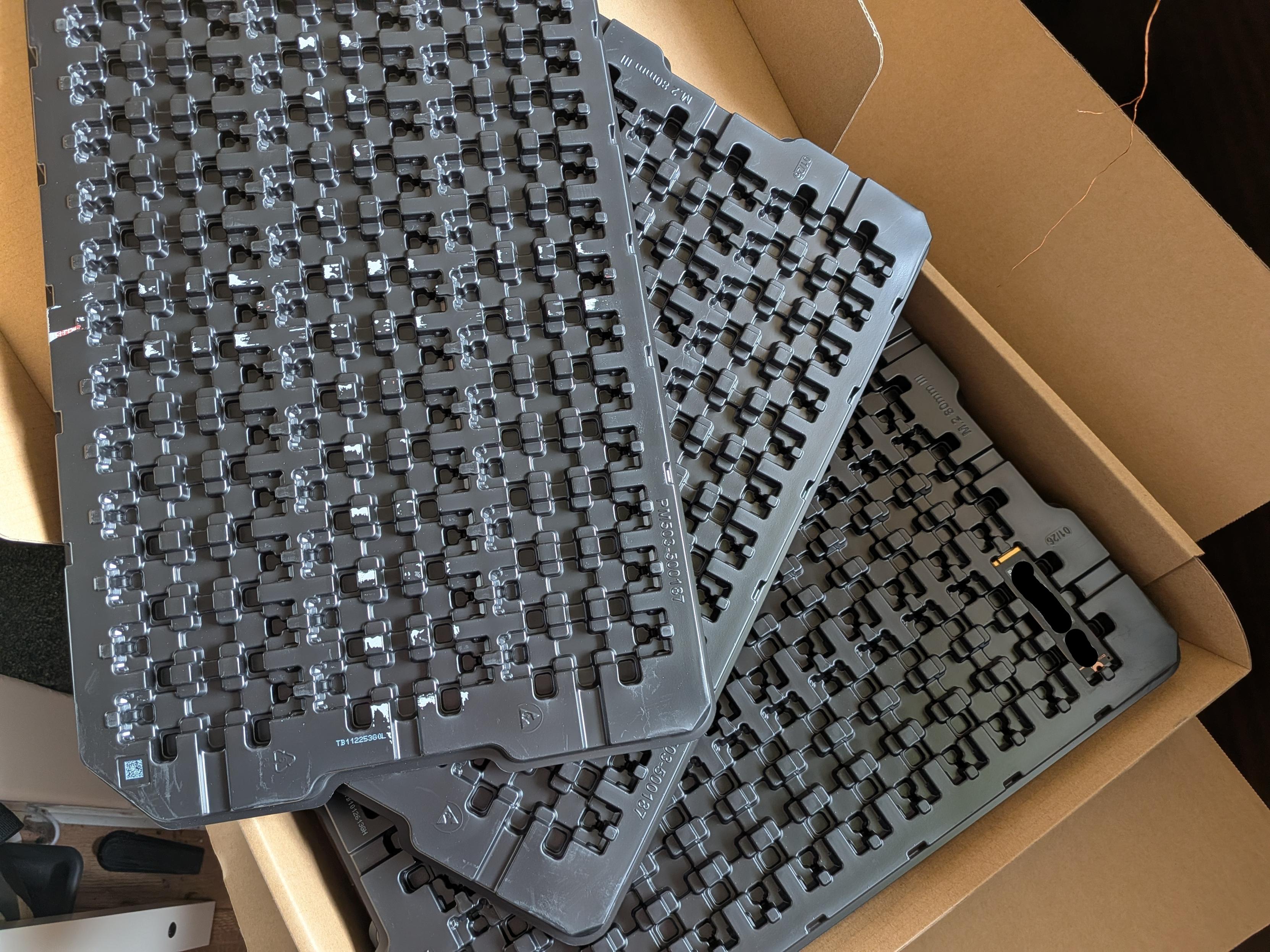 A single SSD sits in a pile of black plastic trays that hold up to 36 NVMe drives each