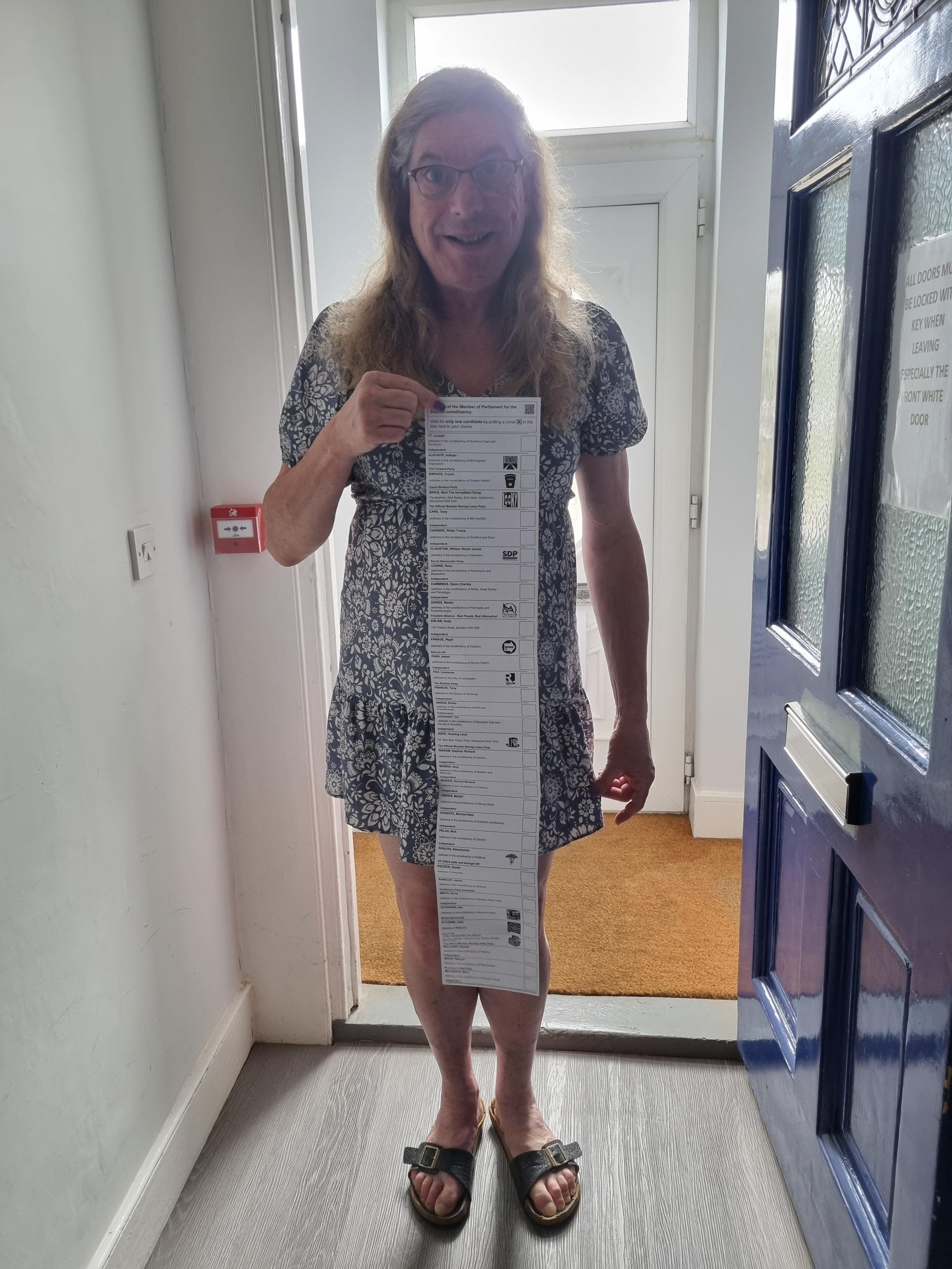 A woman is stood in a doorway holding a long ballot paper