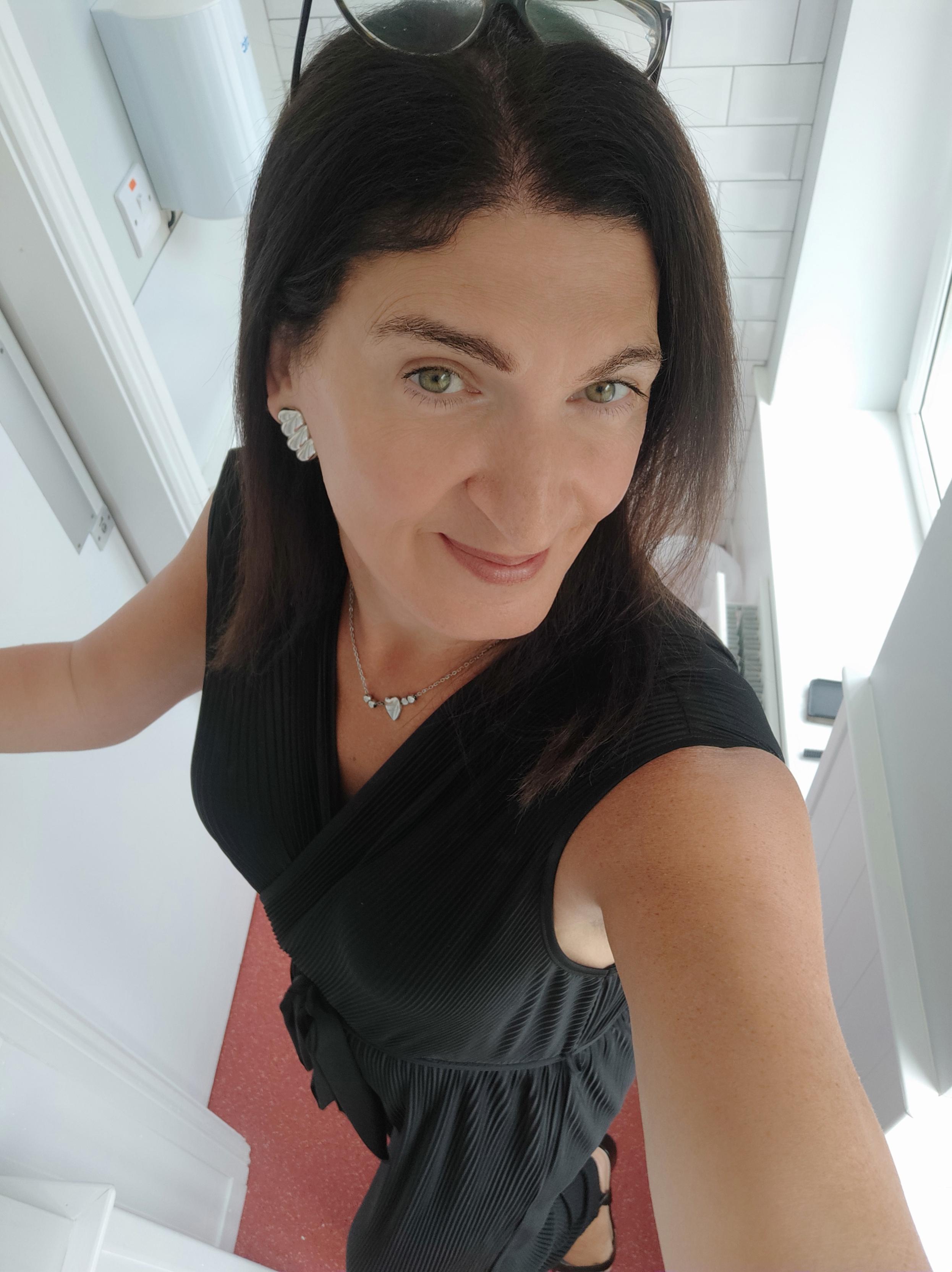 A selfie of a brunette woman in a long flowy black jumpsuit