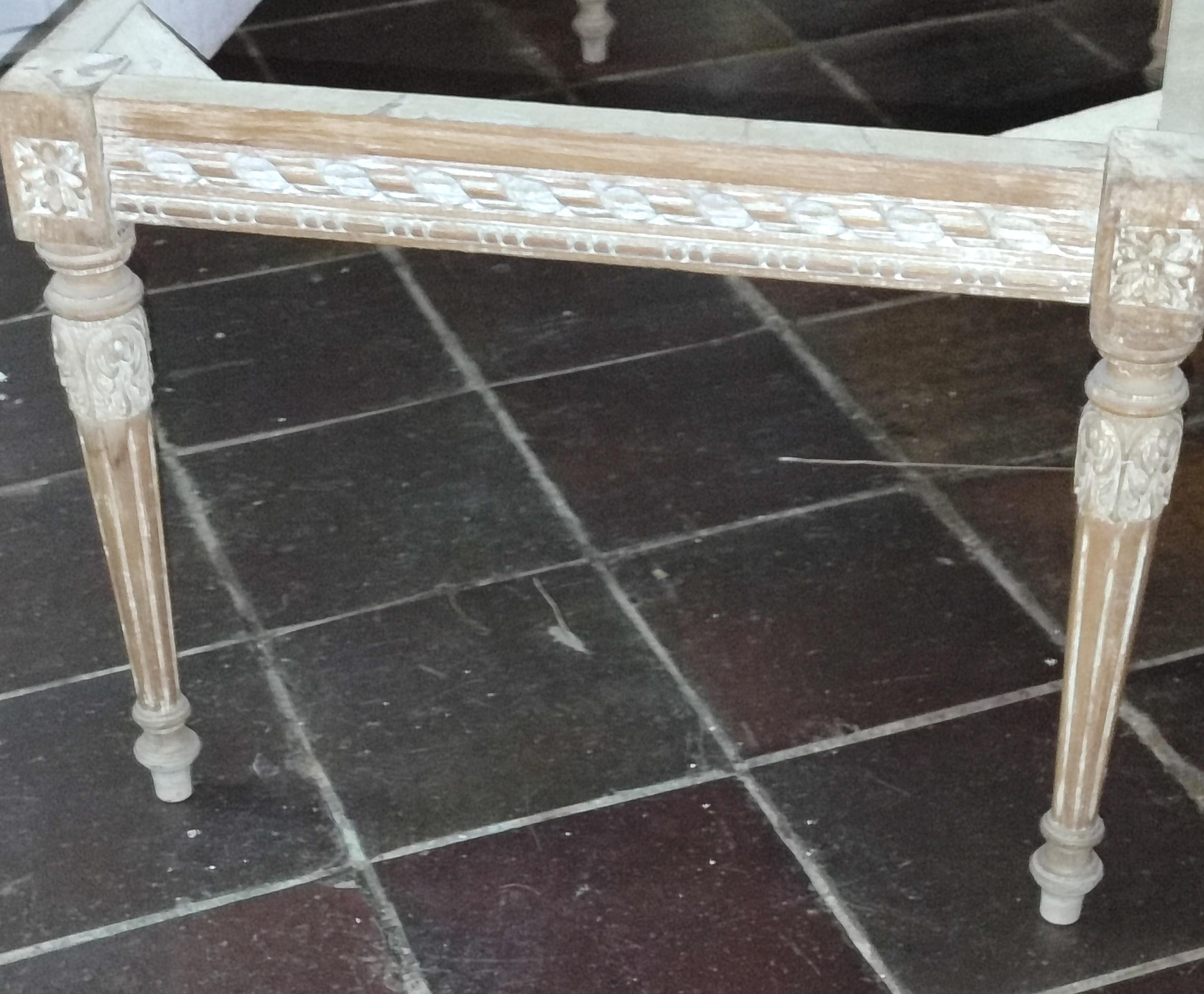 Lateral de la mesa de centro de madera clara, en la que se ven patas de madera troncocónicas invertidas con volutas abajo y acanaladas, talladas con flores en su parte superior. La tabla que une ambas patas también está tallada con pequeñas acanaladuras y elementos geométricos. Tras lijar hasta hartarme, la mesa ha quedado de un color marrón tirando a rosáceo, con todos los detalles tallados blancos, por las tropecientas capas de pintura que tenían antes. Puedo decir que me gusta el efecto, a la vez de afirmar que mi capacidad de lijar ha llegado a su límite.